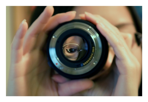 Photograph with hands, face, and camera lens.