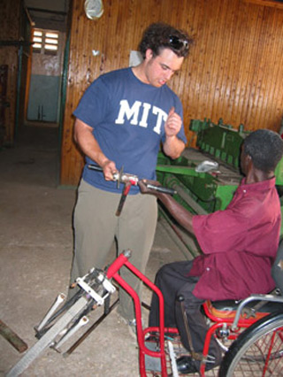 Man sitting in a three-wheeled chair, holding the hand crank component.