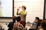 An instructor balances a ruler with weights on his finger, as students look on.