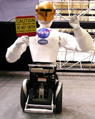 Humanoid robot holding a sign that reads 'Caution: robot operation area. Do not enter.'