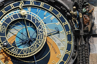 Photo of an ornate clockface with sun and moon hands, adjacent to statues of a skeleton and musician.