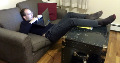 Dr. Short typing on a couch in a room with his home, slouched down with the computer close to his eyes.