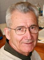 A headshot of Prof. Wit Busza wearing a sweater with a green turtleneck underneath.