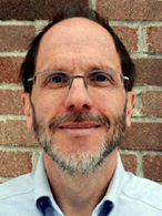 A headshot of Dr. George Stephans wearing a blue button down shirt, open at the collar.