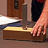 A tuning fork sits on a block of wood.  The professor holds down one end with his hand.