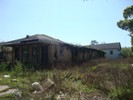 An abandoned long narrow house located in an abandoned field filled with junk.