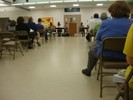 People sit in folding chairs as they listen to a someone speaking at a podium.