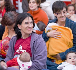 A photograph of a group of women sit on the ground nursing their babies.