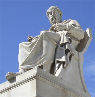 Statue of Socrates sitting, clear blue sky in background.