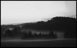 Photo of wooded hills beyond an open field with mist settled low to the ground.