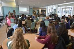 Girls are sitting around round tables listening to a keynote lecture.