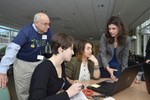 Girls sit around a laptop, and volunteers are talking to them.