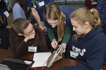 An adult volunteer is helping two girls attach a pressure sensor to the bottom of of a shoe.