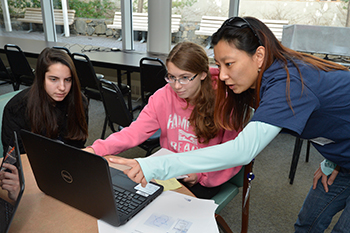 Three women working together on a laptop computer.